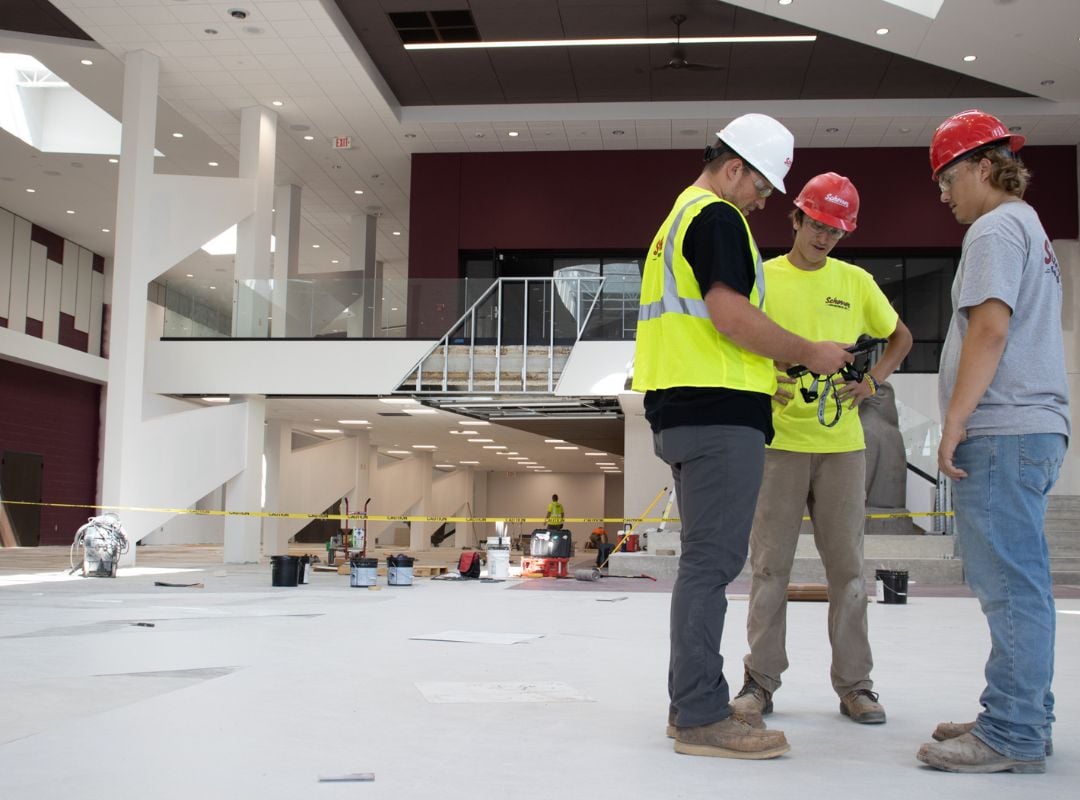 Three Scherrer Construction workers inside a large municipal project confer on designs on a digital tablet. 